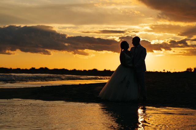 Les silhouettes d’un couple au bord de l’eau, dans le reflet doré du soleil.