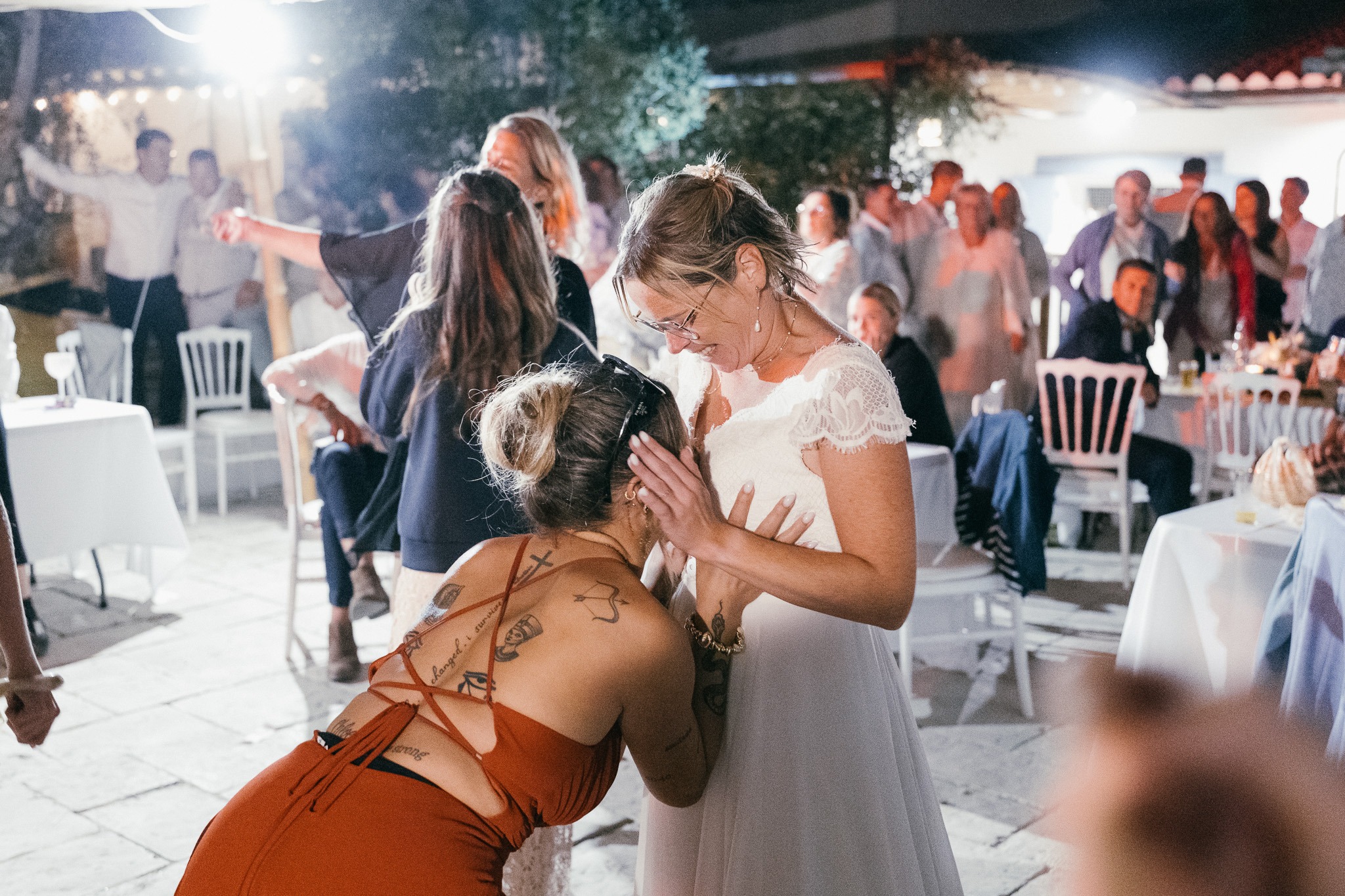 The bride laughs with her guests during the reception, among the lit tables.