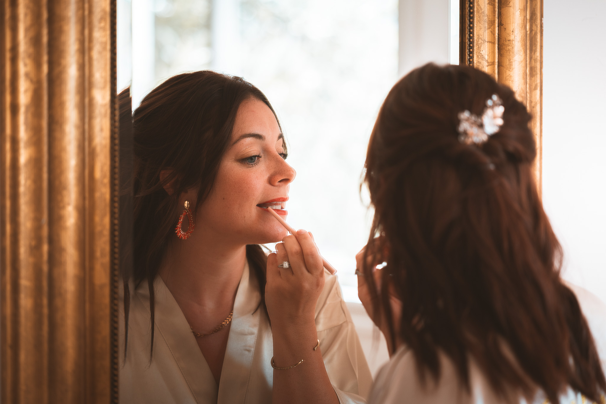 The bride puts the finishing touches to her makeup in a mirror, in soft light.