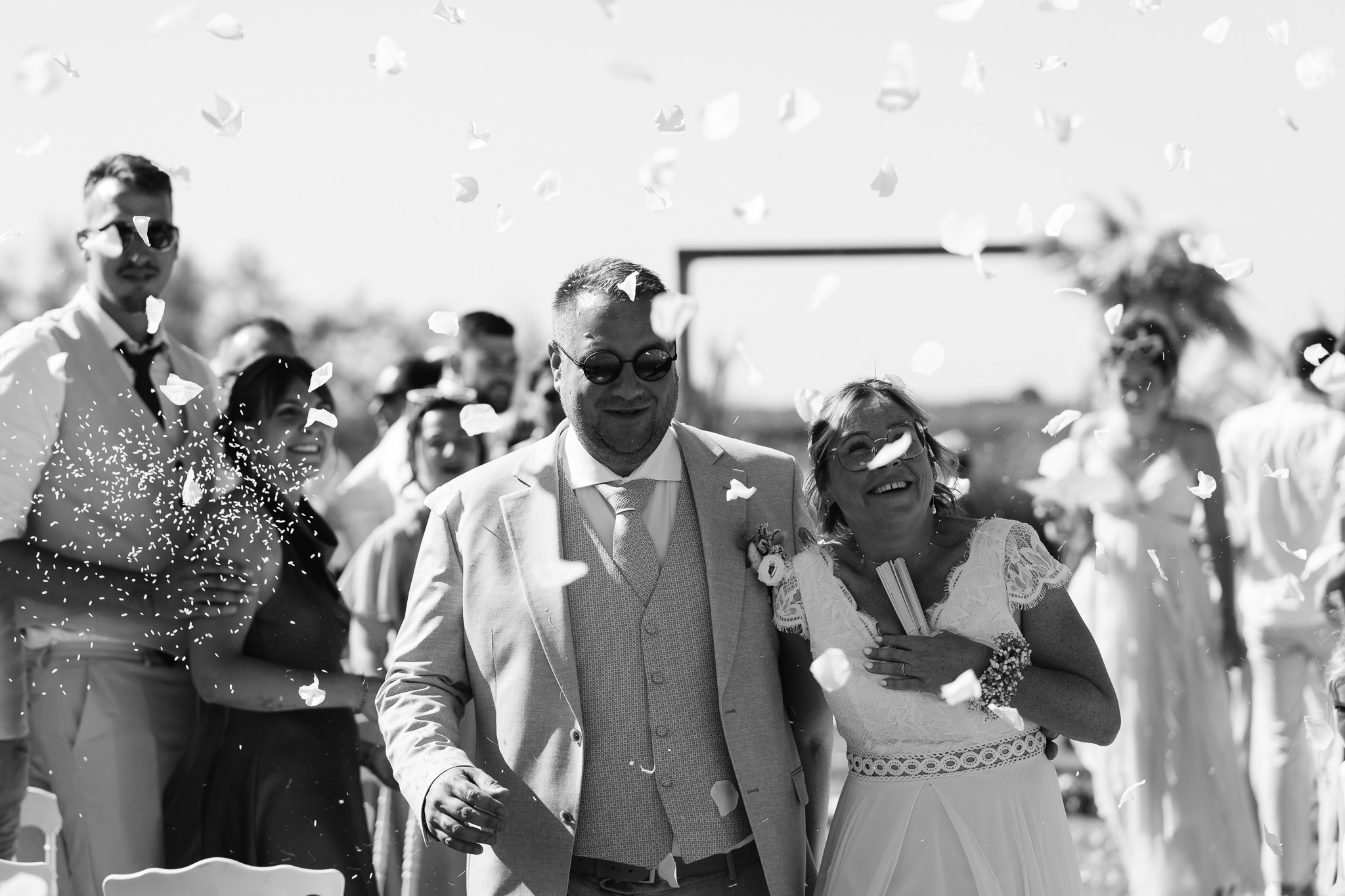The newlyweds walk through their guests under falling confetti, in black and white.