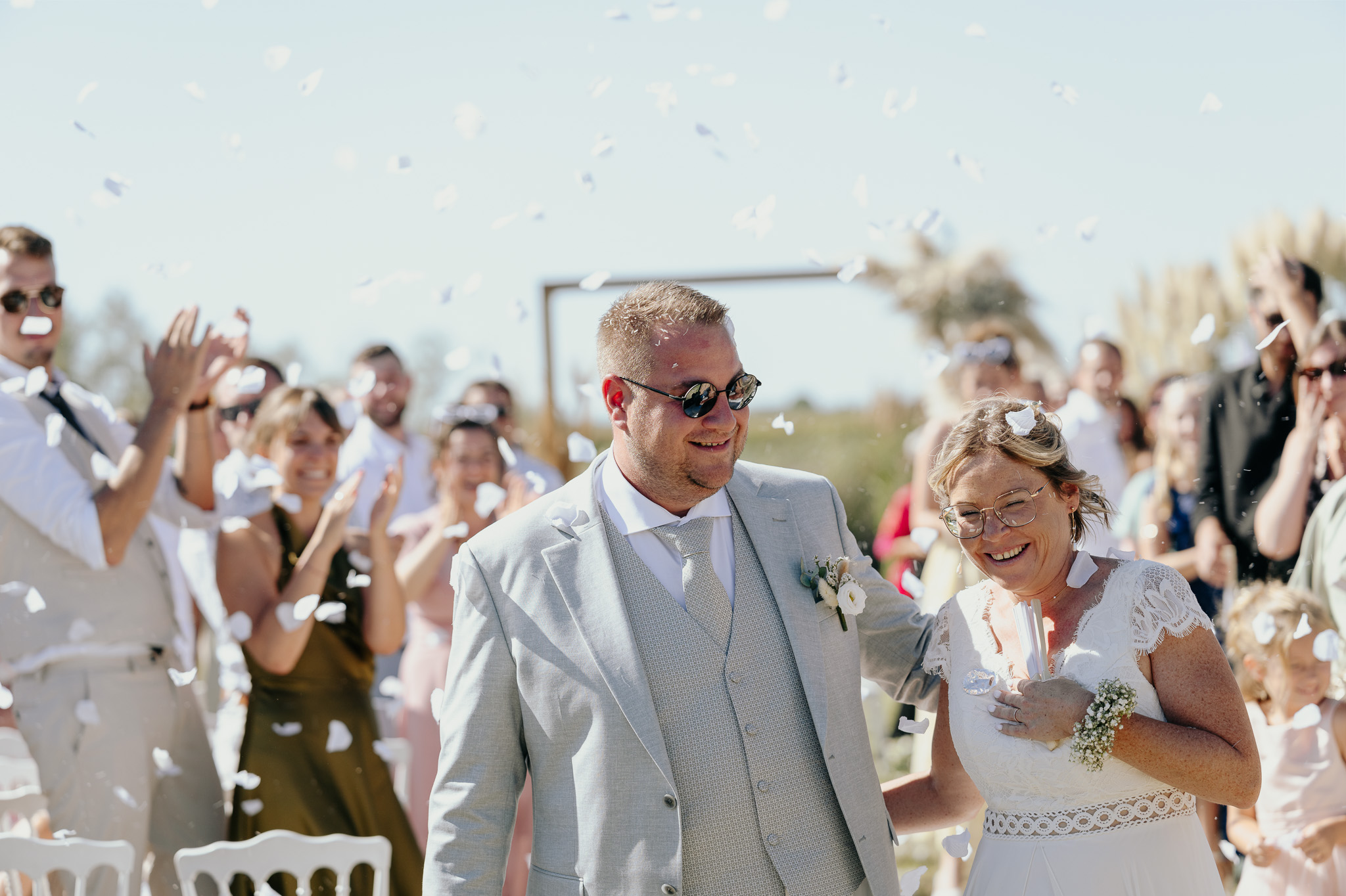 The newlyweds smile beneath confetti, surrounded by their guests.
