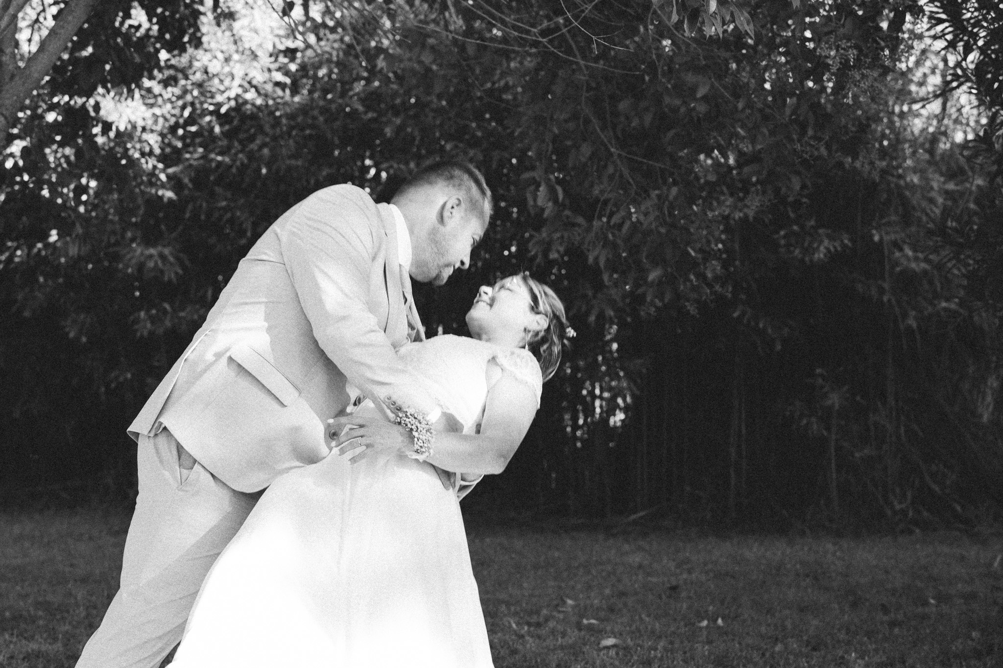 The groom leans down to kiss the bride in his arms, in black and white.