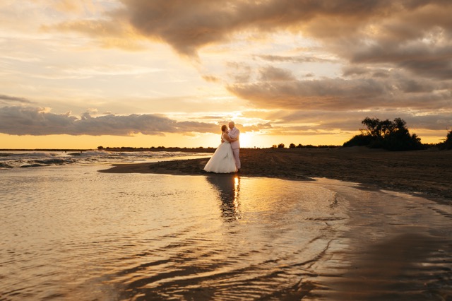 The couple at the water’s edge, between the horizon and the sunset reflections.